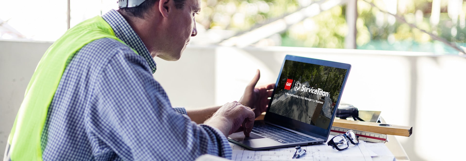 Roofing contractor at a construction job site viewing ServiceTitan on a laptop. 