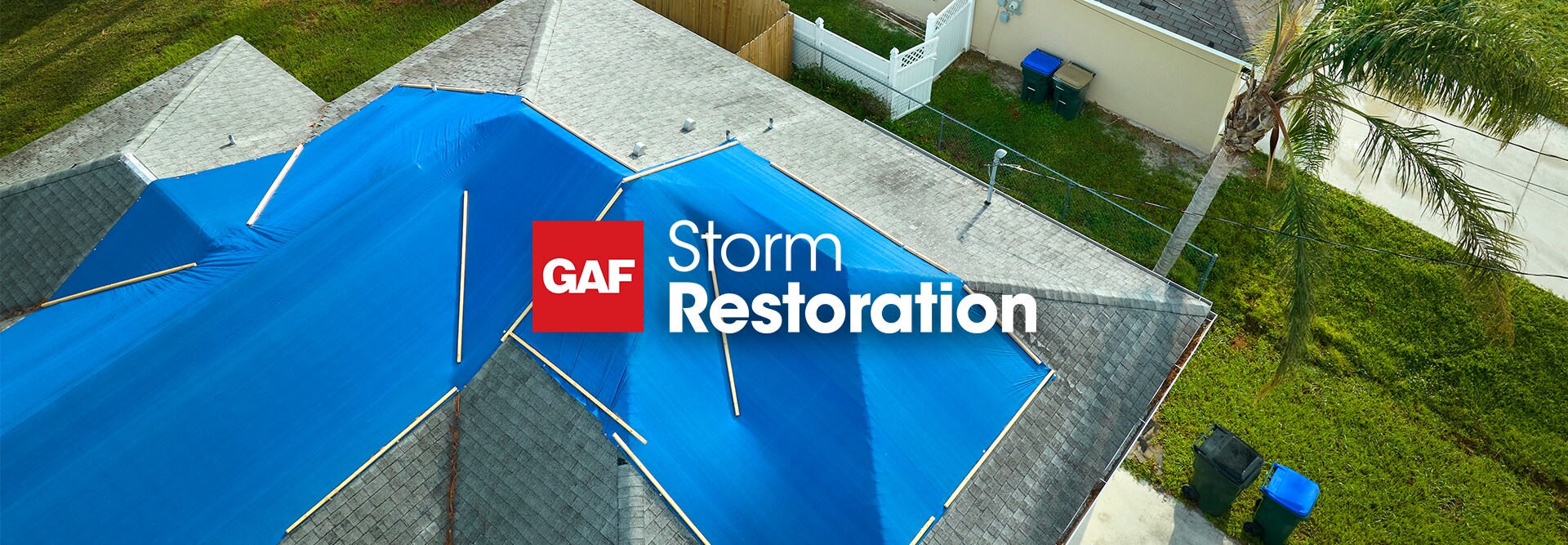 Aerial view of a home with a large blue tarp covering a damaged roof, featuring the GAF storm restoration logo at the top of the image.