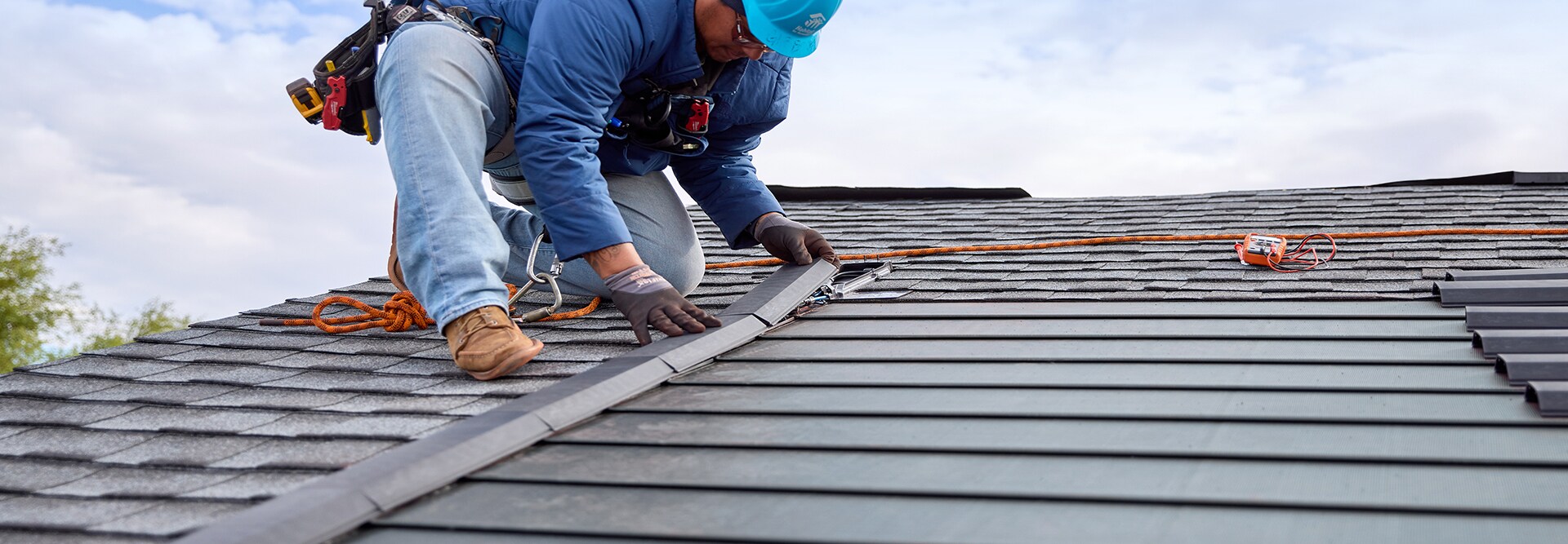 A roofer installng the Timberline Solar roofing system on top of a slate colored asphalt roof