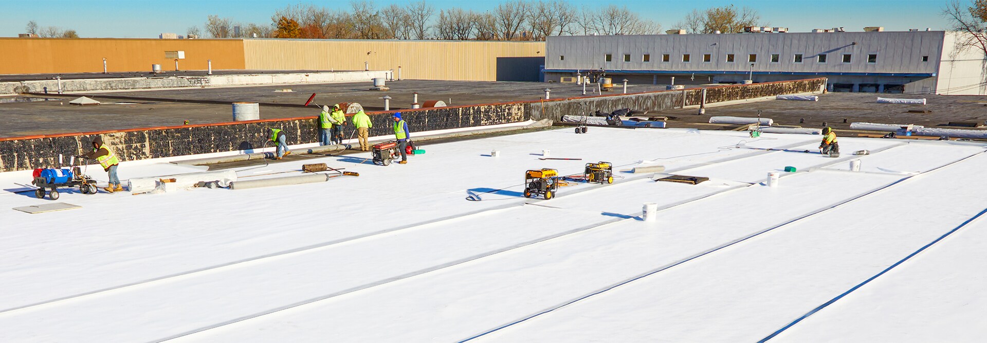 Expansive view of a massive white TPO commercial roofing installation with carts and equipment.