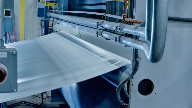 Large-scale industrial machinery manufacturing a continuous white sheet of GAF EverGuard® PVC roofing membrane.