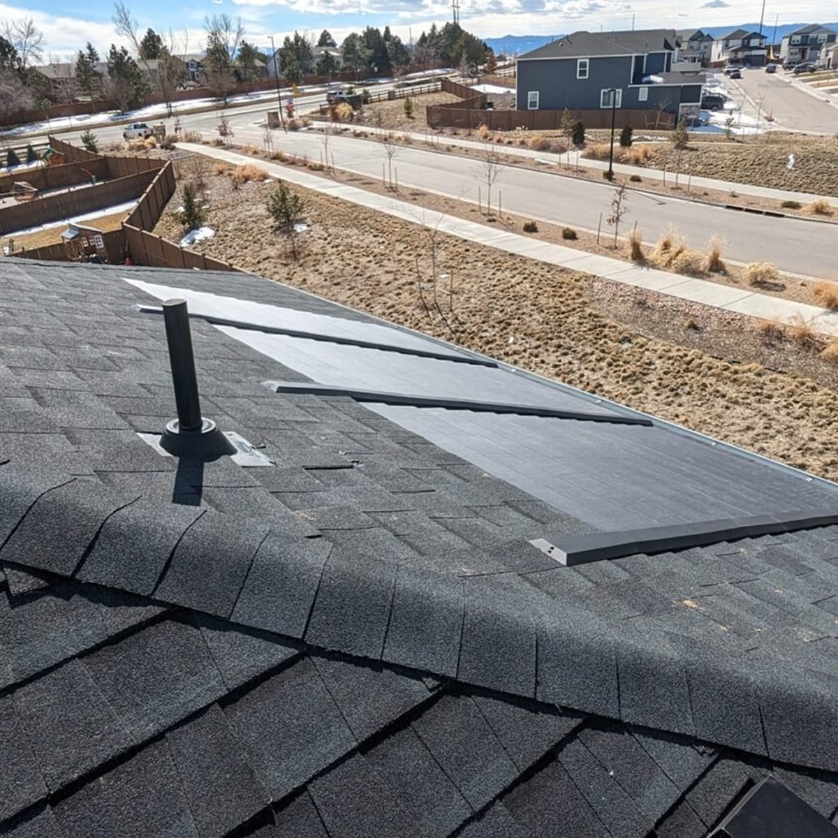 A close-up aerial view shows a residential roof with Timberline Solar® ES 2 shingles, with a suburban street and other houses visible in the background.
