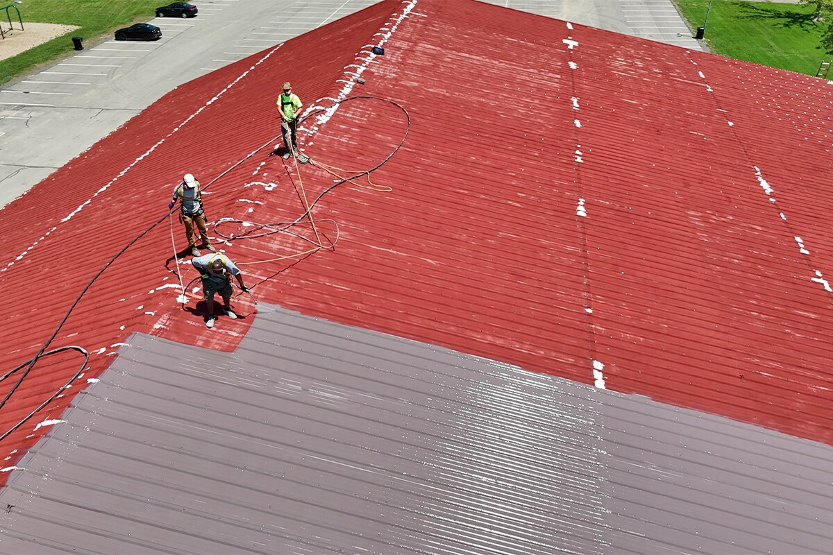 Commercial Roofing Contractors on top of the Elyria Ice Rink removing the old red coating and adding a restorative silicone coating solution from GAF.