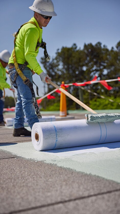 A GAF contractor applying acrylic coating on a flat roof