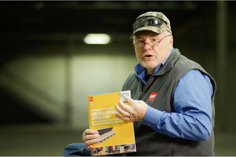 Dave Scott holding up a physical copy of GAF Everguard TPO/PVC Mechanically Attached Roofing System Overview and General Requirements Manual. 