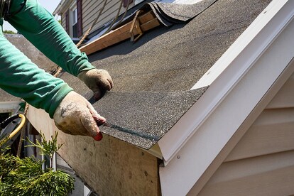Roofer trimming and positioning first starter strip shingle at roof eave.