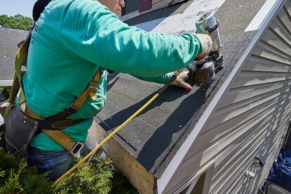 Installing starter strip shingles along roof rake edge with nail gun.