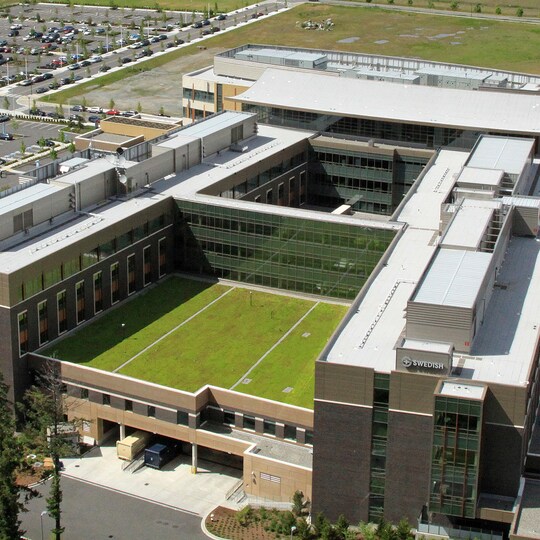 A high-angle view of a modern healthcare complex featuring a sustainable green roof courtyard within its structural layout.