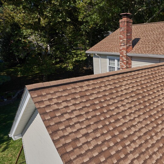 A close-up view of a professionally repaired brown shingle roof, showing architectural shingles near a brick chimney.