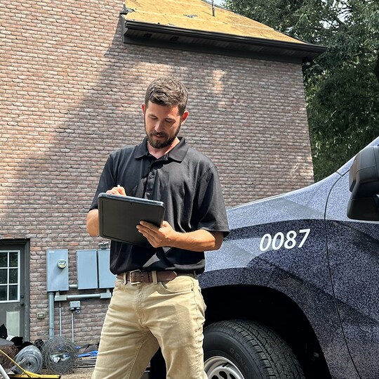 A contractor standing next to a company truck, conducting an inspection and taking notes after storm damage.