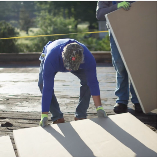 Two GAF certified contractors working together to precisely align and install heavy-duty roof insulation boards.