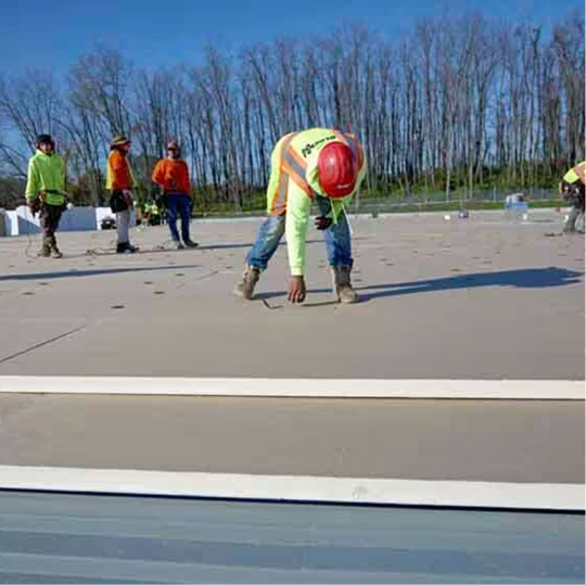 A GAF certified contractor preparing a flat roof deck for insulation installation, with team members in the background.