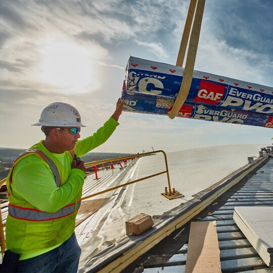 Close-up of a GAF certified commercial roofing contractor helping load rolls of GAF Everguard PVC onto a flat roof.