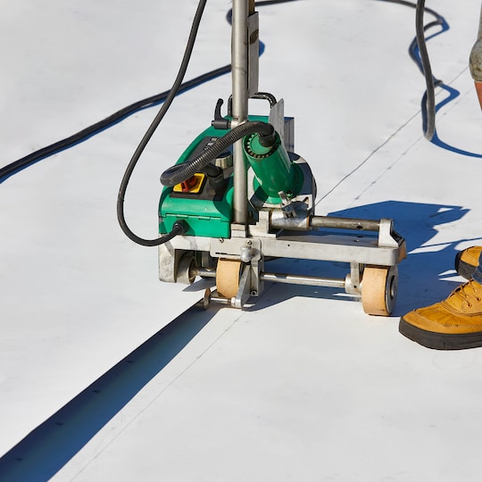 Close-up of an automatic hot-air welding machine seaming a white TPO membrane.
