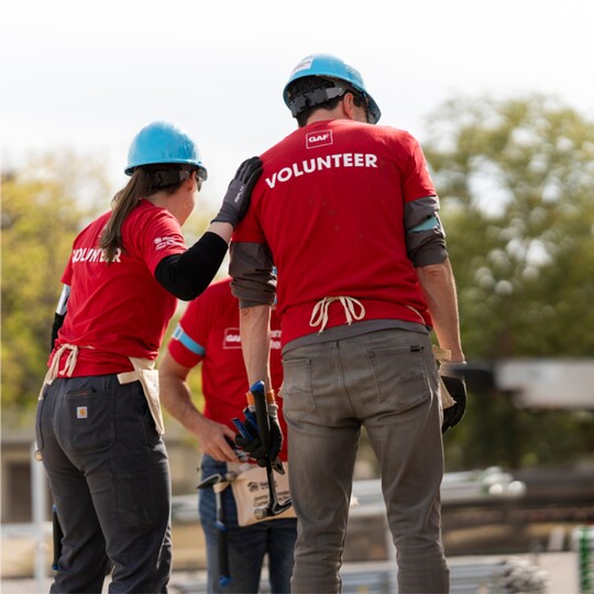 Two contractors wearing GAF-branded t-shirts that say “volunteer” at a job site.
