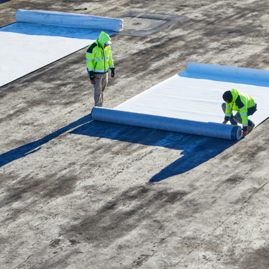 Contractors installing EverGuard® Fleece-Back single-ply membrane on a flat commercial rooftop.
