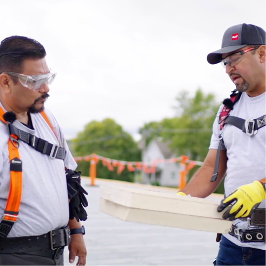 Chino Alvarado y Mitos Fuentes inspeccionan una placa aislante durante una instalación de modernización con TPO de un techo metálico.