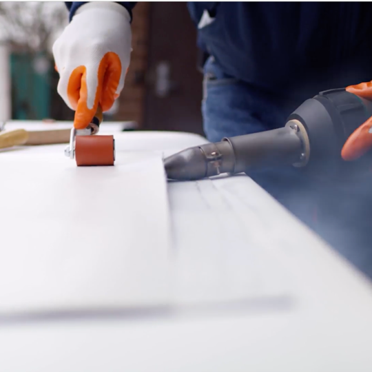 Primer plano de un contratista Certified™ de GAF adhiriendo una membrana de PVC EverGuard con un rodillo manual y una soldadora de aire caliente.