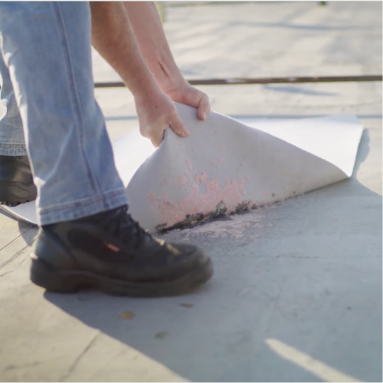 A GAF certified contractor lifting a TPO membrane sheet during a modified bitumen roof recover project.