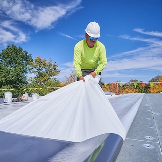 A contractor unrolls a roll of roofing material made by GAF on a commercial worksite. 