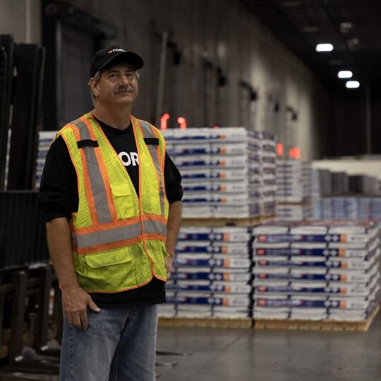 GAF roofing employee in front of stacks of shingles in packages.