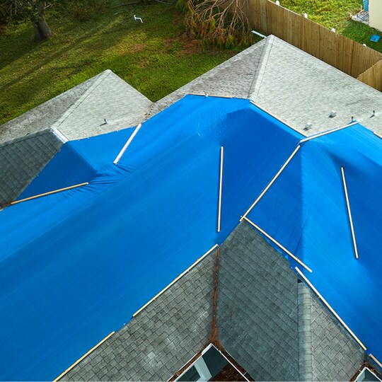 A light green roof partially covered by  blue tarps to protect it from storm damage.