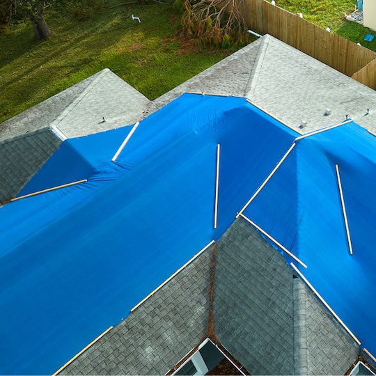 A light green roof partially covered by  blue tarps to protect it from storm damage.