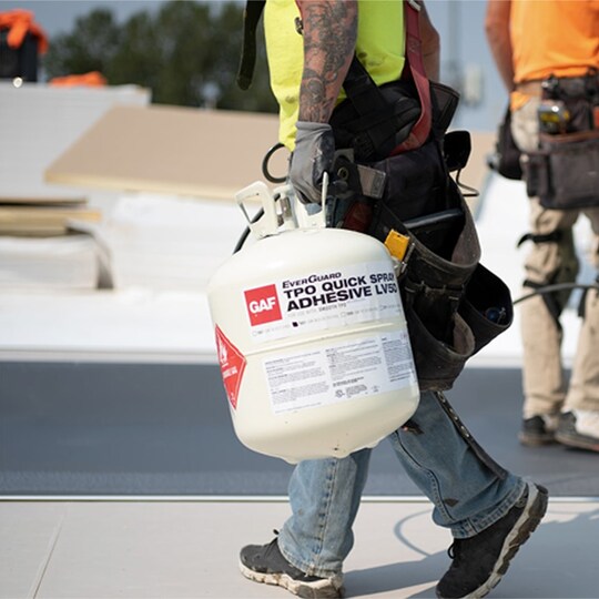 Roofers install GAF EverGuard® TPO Quick-Spray Adhesive on a flat roof
