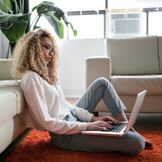 women sitting on floor in living room searching on laptop