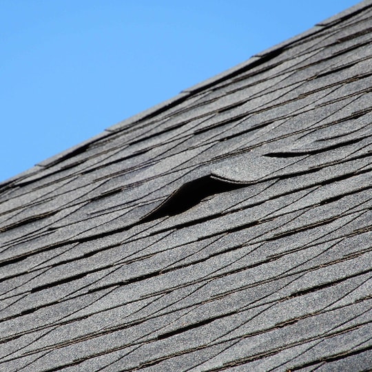 Aged shingles on a roof, showing a gap where leaks can come from. 