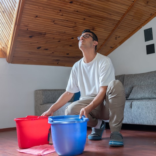 A man using buckets to catch dripping water from a leaking roof. 