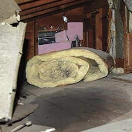 Damaged and wet attic with rolled up insulation