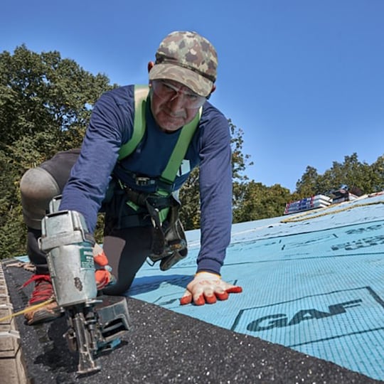 A roofer installing starter shingles on the edge of a roof.