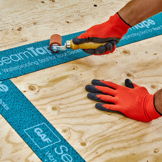 Roofer using roller to install GAF Roof Deck Seam Tape