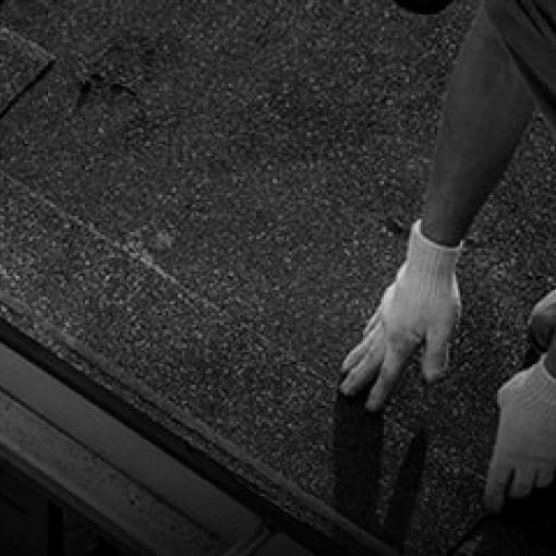 Shaded image of a roofer with white gloves installing GAF roofer strip shingles to prevent shingle blow-off