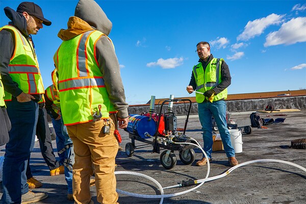 A group of three GAF certified roofing professionals in safety vests collaborating on a commercial roof.