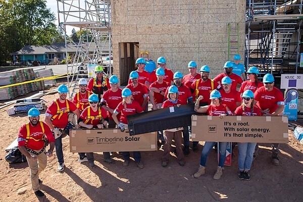 A group of GAF volunteers in blue hard hats and red shirts posing for a photo at a job site.