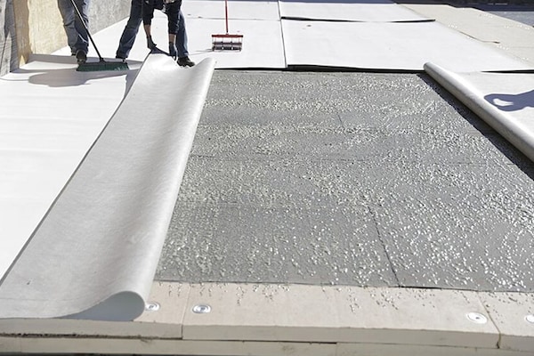 Two GAF certified commercial contractors adhering commercial roofing materials onto a flat roof.