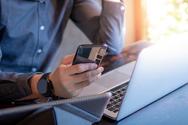 Man sitting at desk with cell phone and laptop.