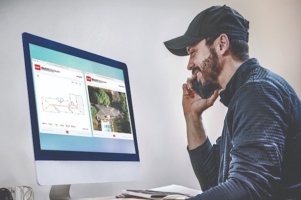 Side view of a man reviewing a computer monitor that displays a detailed roof diagram and an aerial photo from GAF QuickMeasure roofing reports.