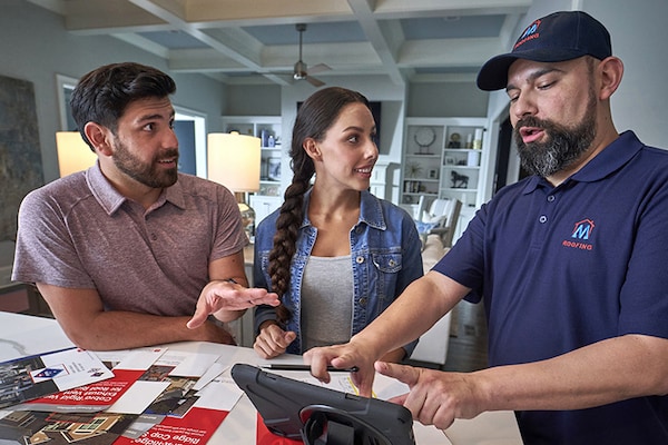 A couple discusses roofing options with a GAF certified contractor at their home. 