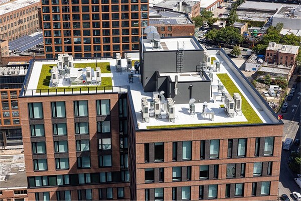 Aerial view of a modern urban commercial building featuring a white membrane roof and green rooftop garden areas.