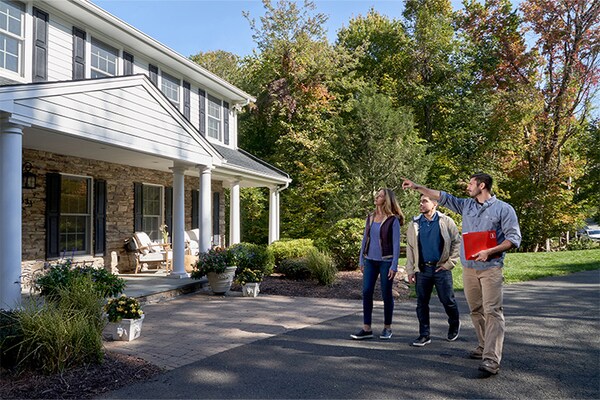 A GAF Certified roofer is speaking with a homeowner couple outside their house about the repair plan for their storm-damaged roof.