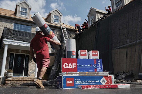 A GAF certified contractor walking past a stack of GAF roofing supplies in front of a house.