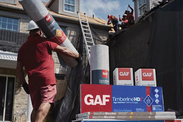 GAF residential roofing materials outside home with roofer holding rolled product