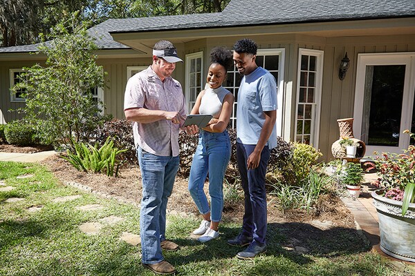 A GAF certified contractor explaining warranties documentation to a homeowner couple outside of their house.