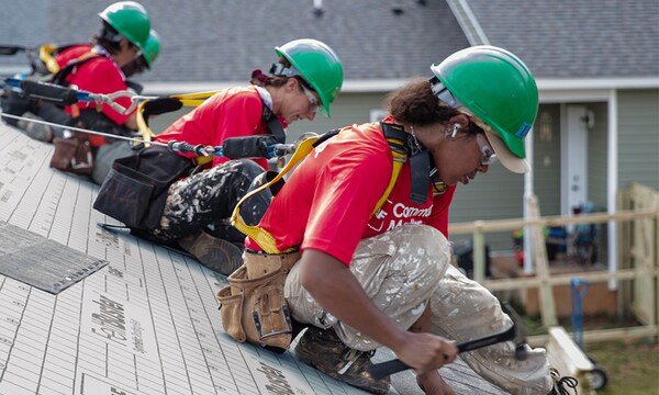 Volunteers wearing red t-shirts with The “Community Matters” logo on them work on a rooftop. 