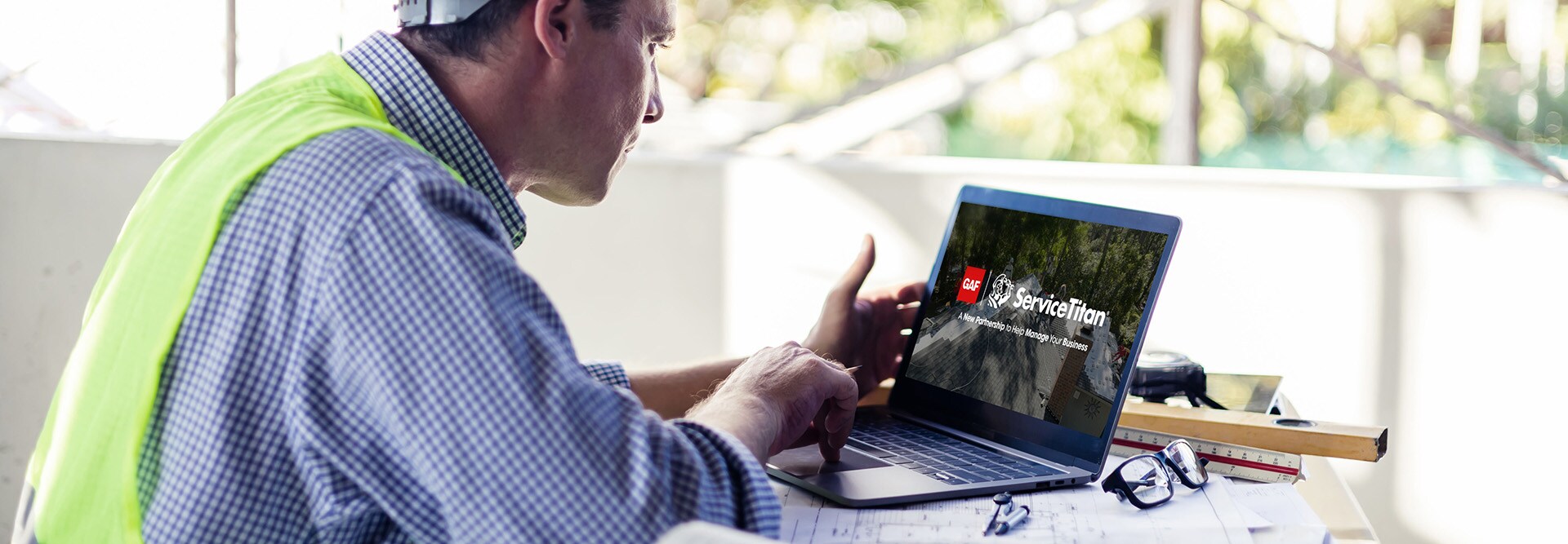 Roofing contractor at a construction job site viewing ServiceTitan on a laptop. 