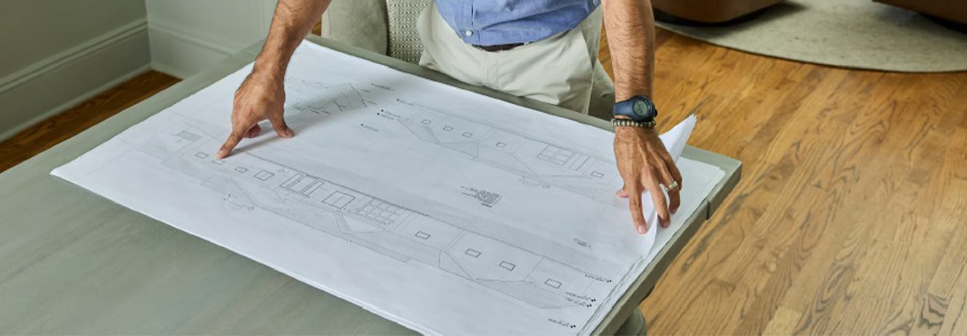 A man reviewing architectural drawings of a home and roof inside an office with a circle of arm chairs.