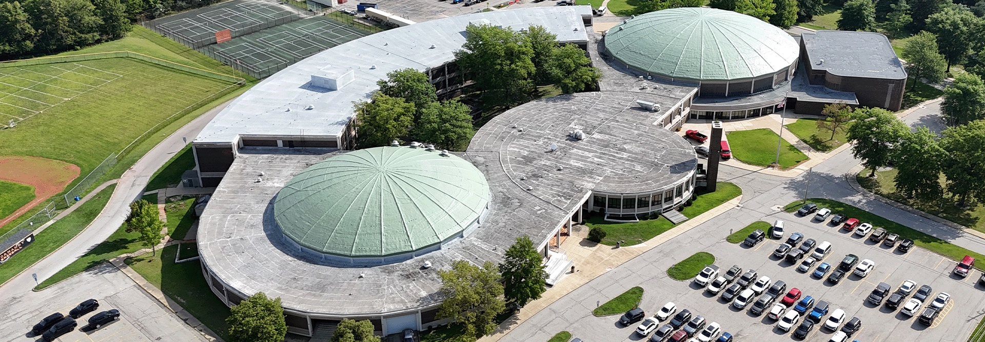 Aerial view of Normandy High School in Parma, Ohio showing worn Patina Green domes and classroom wing roofs before GAF silicone coating restoration